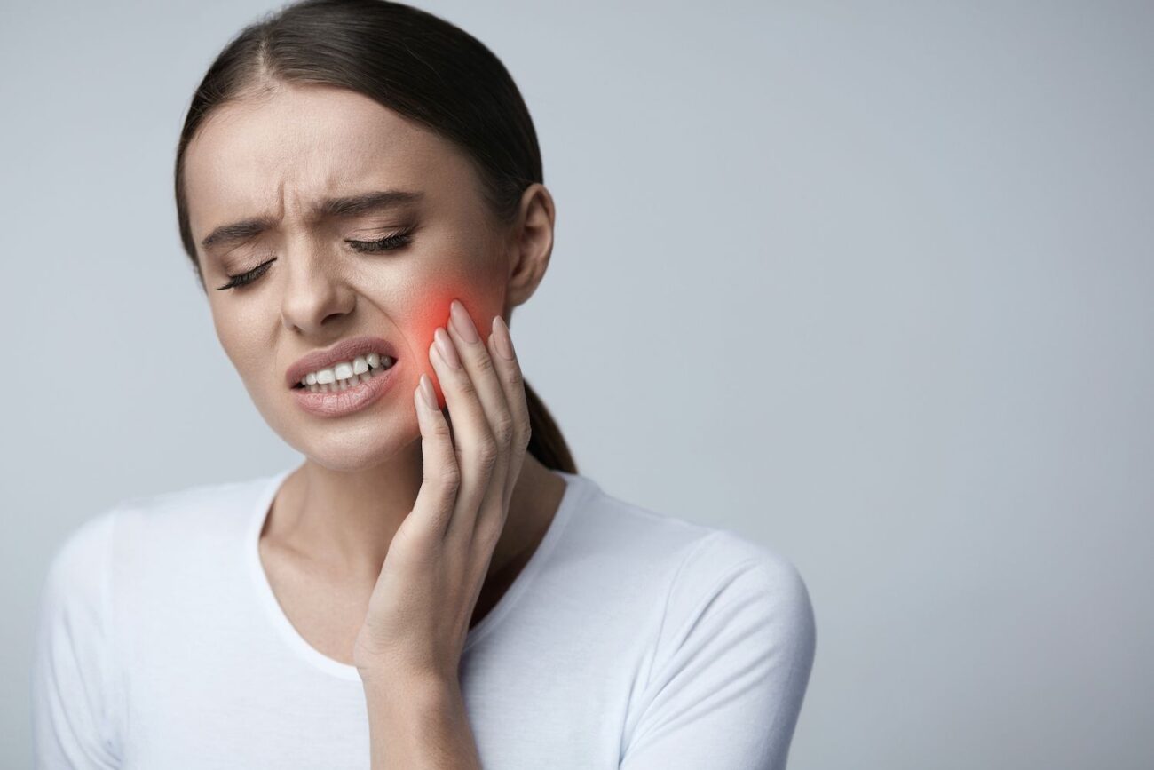Woman experiencing tooth pain, holding her cheek, highlighting the discomfort associated with dental infections and the importance of root canal therapy.